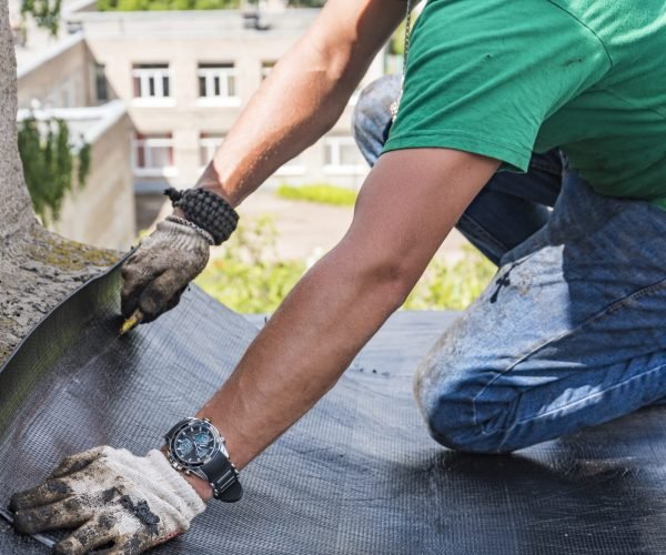 A construction worker cuts waterproofing material and prepares it for installation. Overhaul of the roof of the house.